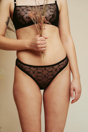 Model holding some dried flowers and wearing the Kauf High Leg Knicker and Bandeaux Wire Bra in black